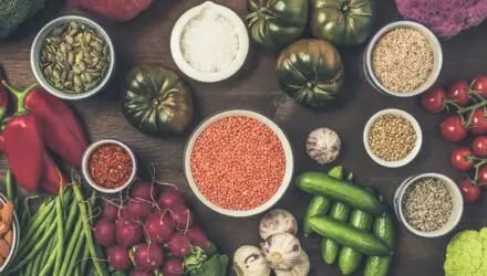 Ingrédients de cuisine végétarienne sur une table en bois sombre, vus de dessus, avec différents légumes et légumineuses.